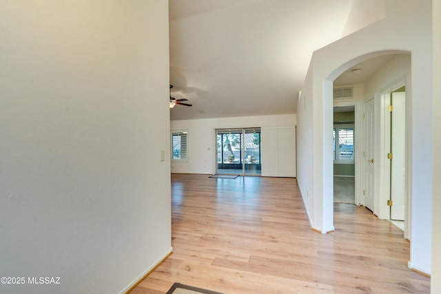 hallway with light wood-type flooring, plenty of natural light, visible vents, and arched walkways