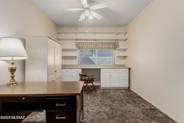 office with dark colored carpet, built in study area, ceiling fan, a textured ceiling, and baseboards