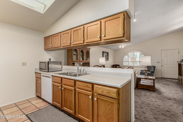 kitchen featuring a peninsula, vaulted ceiling with skylight, white dishwasher, and a sink