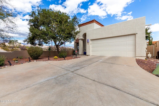 view of front of house with concrete driveway, an attached garage, fence, and stucco siding