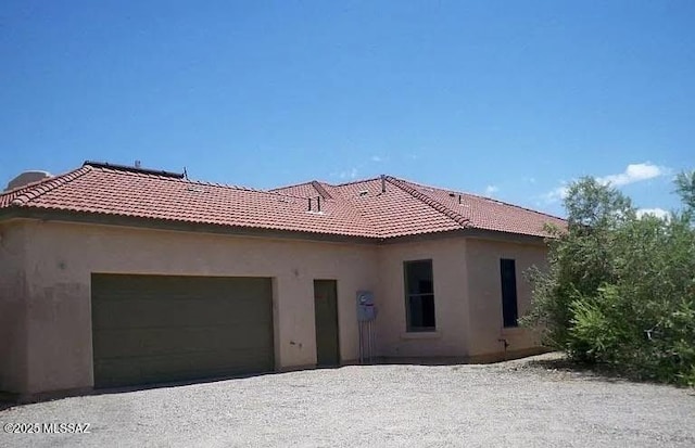 rear view of house featuring a garage, a tile roof, and stucco siding