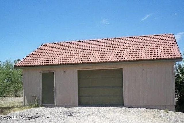 view of side of home featuring a detached garage, an outbuilding, and a tiled roof