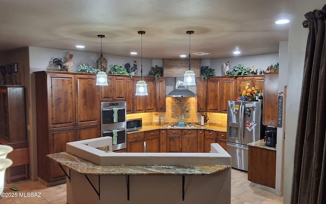 kitchen featuring tasteful backsplash, a kitchen island, brown cabinets, stainless steel appliances, and wall chimney range hood