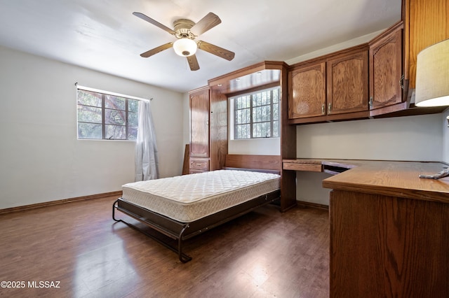 bedroom with built in desk, dark wood-type flooring, and baseboards