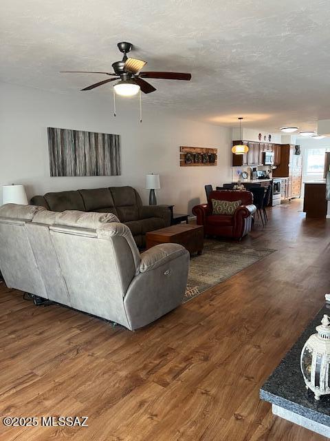 living room with a textured ceiling, a ceiling fan, and dark wood-style flooring