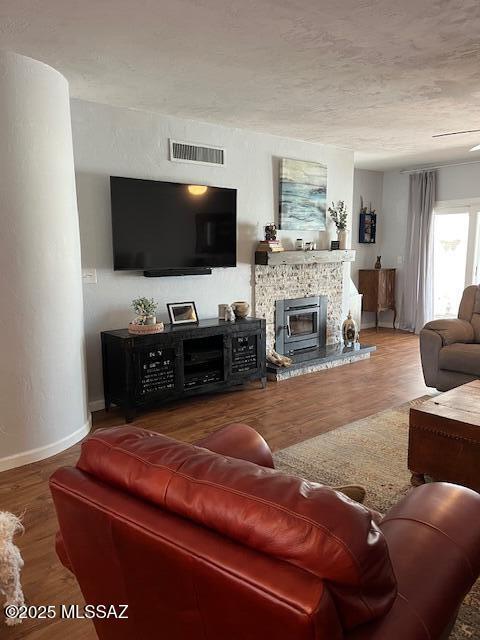 living area with a textured ceiling, wood finished floors, visible vents, baseboards, and a tiled fireplace