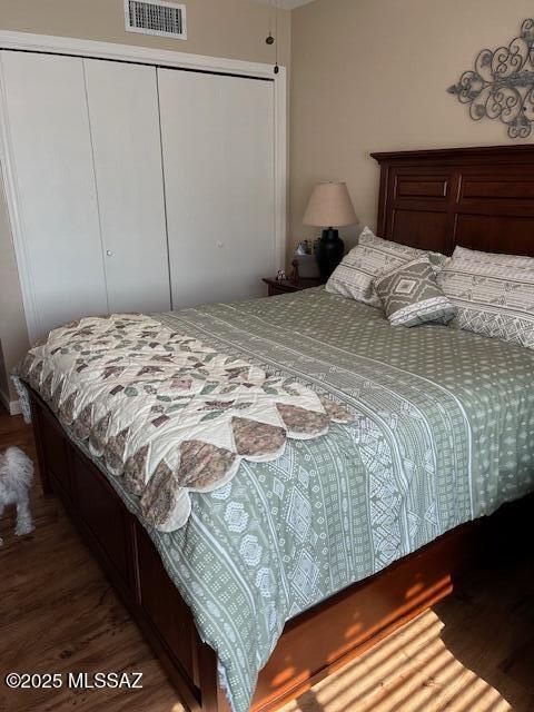 bedroom with a closet, wood finished floors, and visible vents