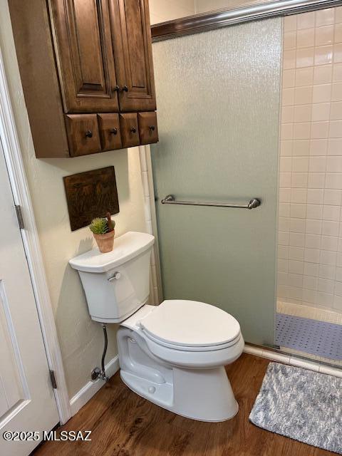 bathroom with a stall shower, baseboards, toilet, and wood finished floors