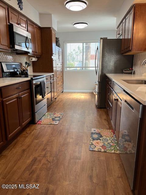 kitchen featuring dark wood-type flooring, a sink, light countertops, appliances with stainless steel finishes, and tasteful backsplash