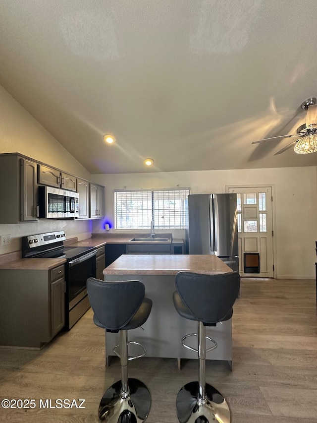 kitchen featuring lofted ceiling, light wood-style flooring, stainless steel appliances, a kitchen bar, and a sink