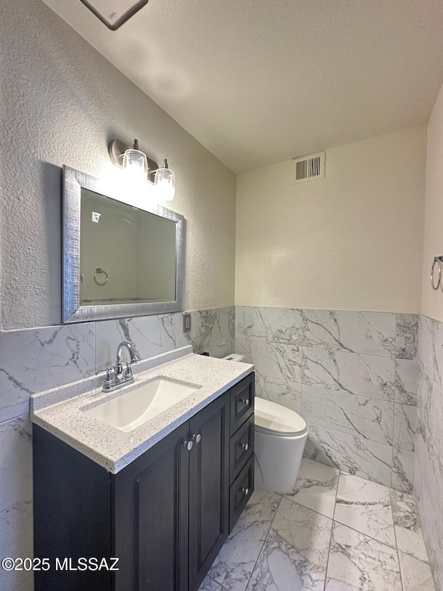 half bath with a textured ceiling, marble finish floor, vanity, and visible vents