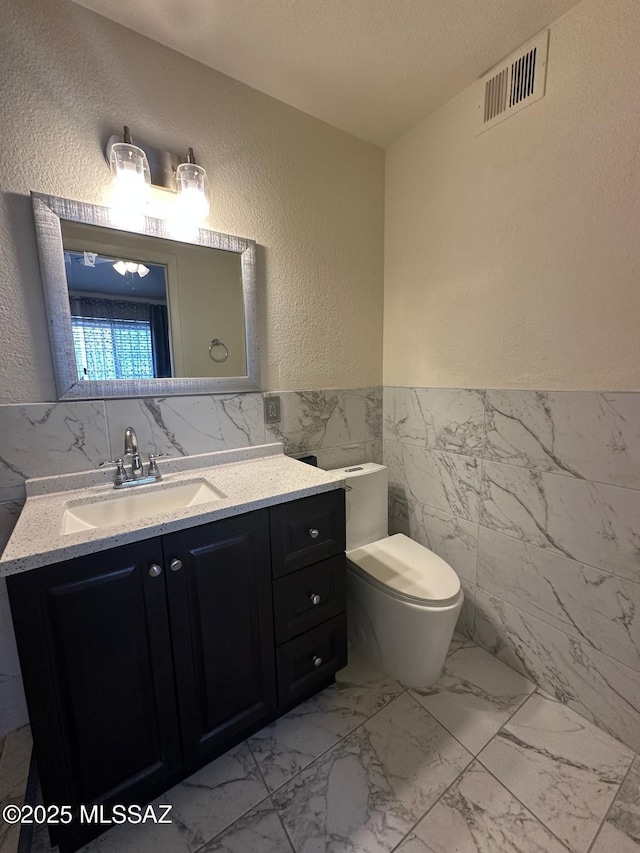 half bathroom featuring visible vents, a textured wall, marble finish floor, a textured ceiling, and tile walls