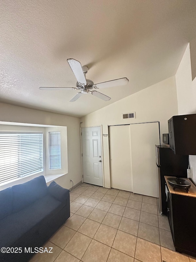 interior space featuring light tile patterned floors, visible vents, lofted ceiling, ceiling fan, and a textured ceiling