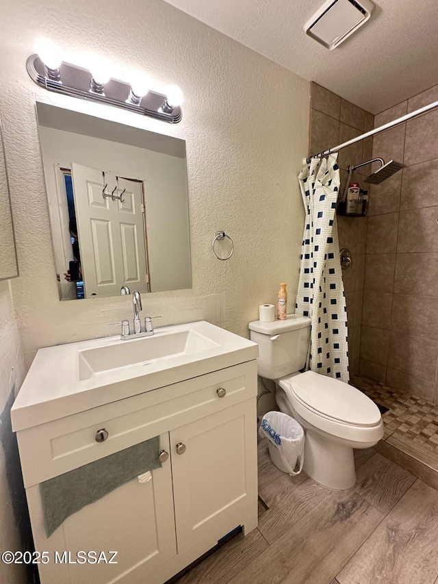 full bath featuring a textured wall, toilet, a tile shower, vanity, and a textured ceiling