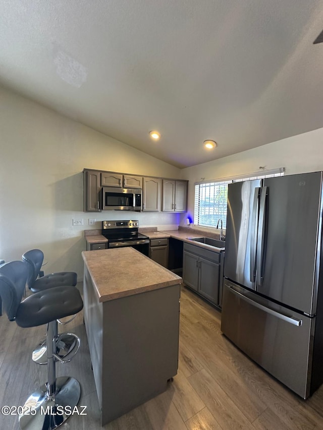 kitchen with stainless steel appliances, gray cabinets, a sink, vaulted ceiling, and light wood-type flooring