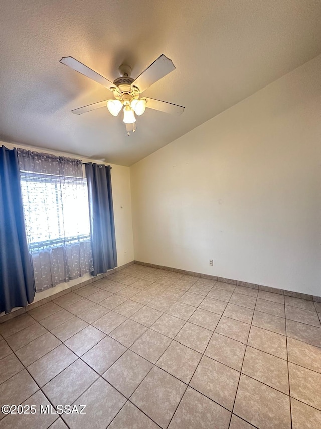 spare room with ceiling fan, baseboards, a textured ceiling, and light tile patterned flooring