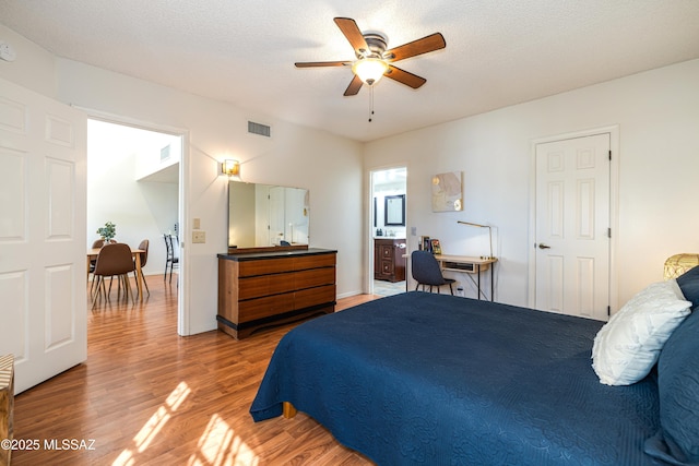 bedroom with ensuite bathroom, visible vents, light wood finished floors, and a textured ceiling