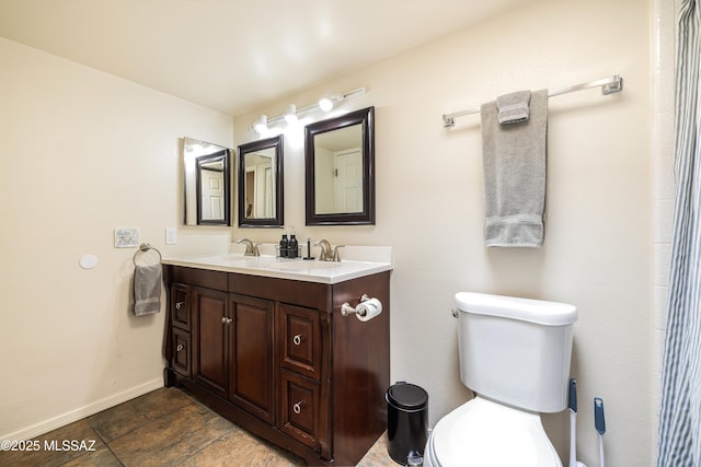 bathroom featuring double vanity, toilet, baseboards, and a sink