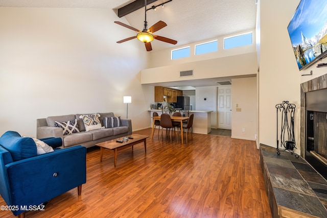 living room featuring wood finished floors, visible vents, high vaulted ceiling, a tiled fireplace, and beamed ceiling