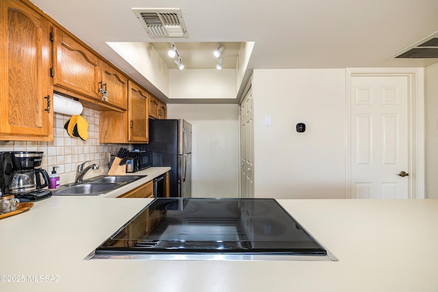 kitchen featuring brown cabinetry, visible vents, a sink, light countertops, and backsplash