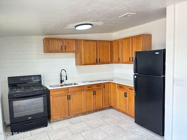 kitchen featuring light countertops, a sink, a textured ceiling, brown cabinetry, and black appliances