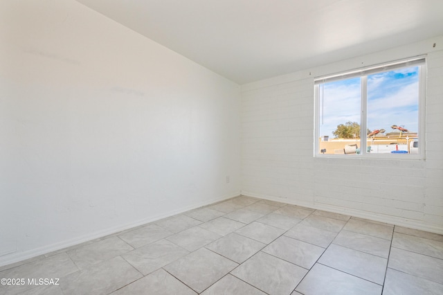 spare room featuring light tile patterned flooring, brick wall, and baseboards