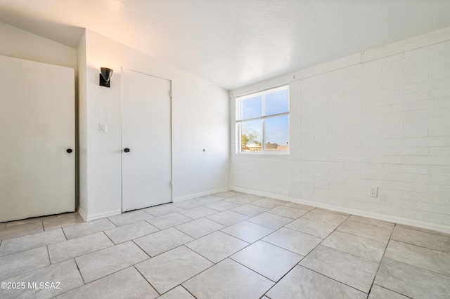 unfurnished bedroom with light tile patterned flooring, brick wall, and a closet