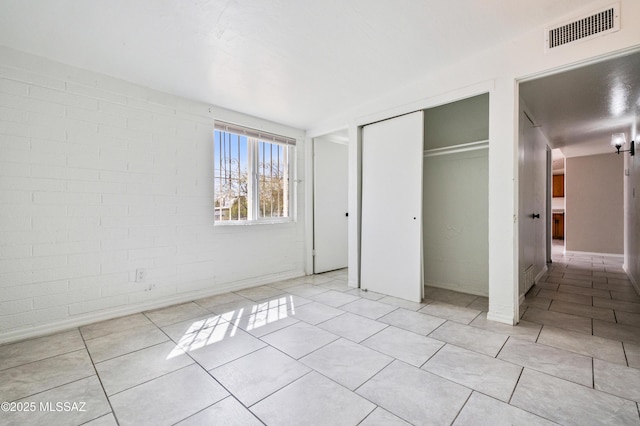 unfurnished bedroom with light tile patterned floors, brick wall, a closet, and visible vents