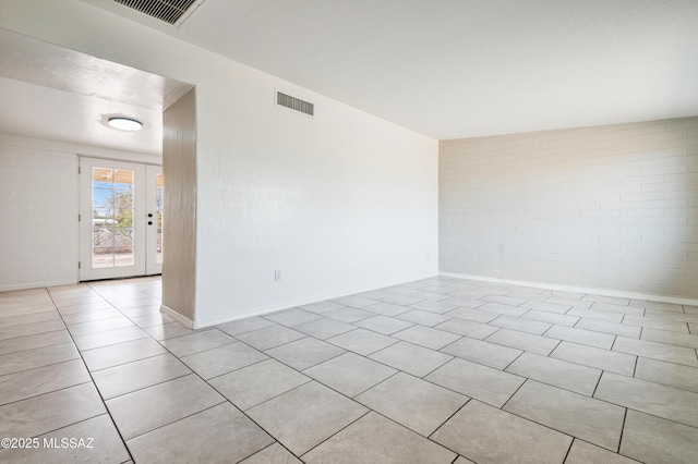 unfurnished room featuring light tile patterned floors, brick wall, and visible vents