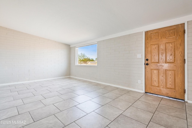 unfurnished room featuring lofted ceiling, brick wall, light tile patterned flooring, and baseboards