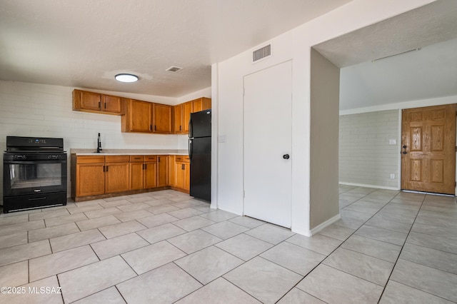 kitchen with light tile patterned floors, light countertops, visible vents, brown cabinetry, and black appliances