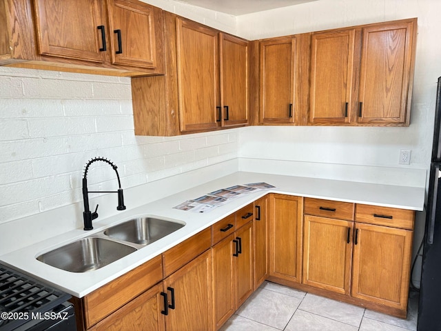 kitchen with light countertops, light tile patterned floors, decorative backsplash, a sink, and brown cabinetry