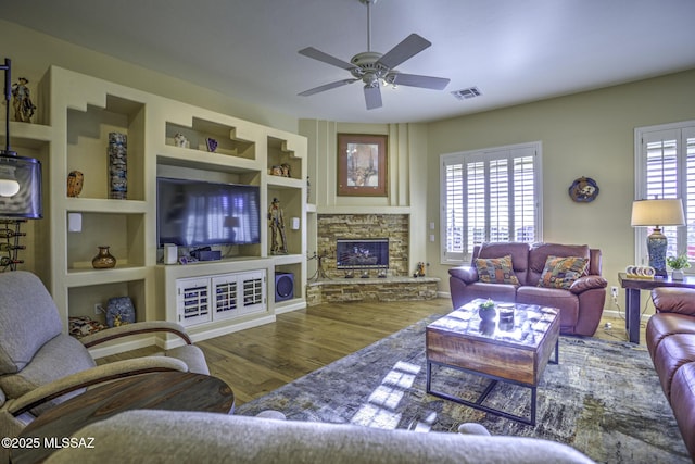13517 N Heritage Gateway Ave, Marana, AZ 85658 - living room featuring visible vents, built in shelves, wood finished floors, a stone fireplace, and ceiling fan