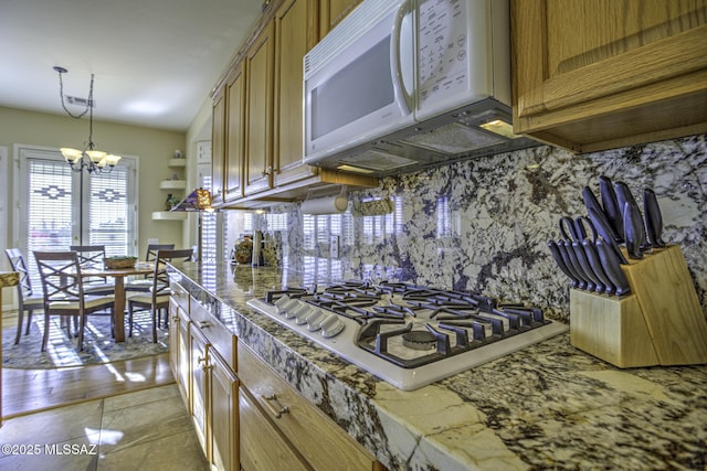 13517 N Heritage Gateway Ave, Marana, AZ 85658 - kitchen featuring white microwave, tasteful backsplash, brown cabinets, stainless steel gas stovetop, and a notable chandelier