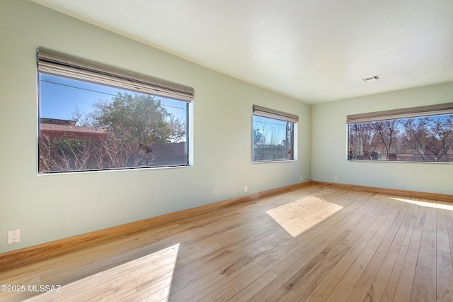 spare room featuring light wood-style floors, plenty of natural light, visible vents, and baseboards