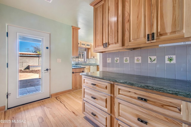 kitchen with light wood finished floors, decorative backsplash, light brown cabinetry, white dishwasher, and dark stone counters