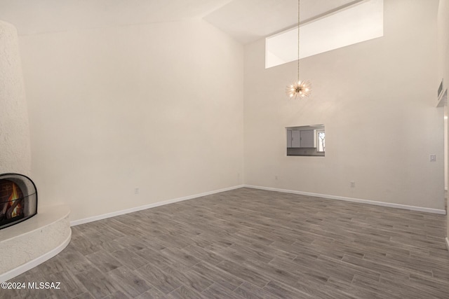 unfurnished living room with a chandelier, a large fireplace, dark wood-type flooring, and baseboards