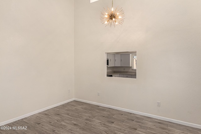 empty room featuring baseboards, a high ceiling, wood finished floors, and an inviting chandelier