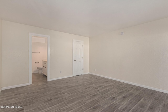 unfurnished bedroom featuring dark wood-style floors, baseboards, and ensuite bathroom