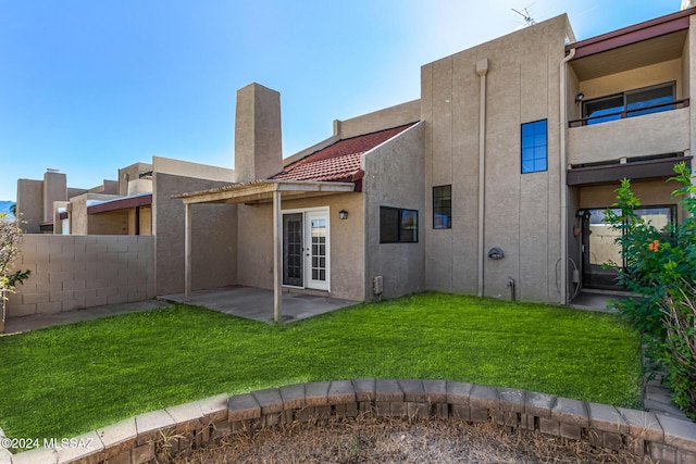 back of property featuring french doors, a lawn, fence, and stucco siding