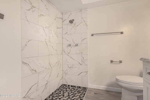 full bath featuring toilet, wood finished floors, vanity, baseboards, and a tile shower