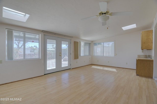 unfurnished living room featuring lofted ceiling with skylight, ceiling fan, light wood-style floors, and french doors