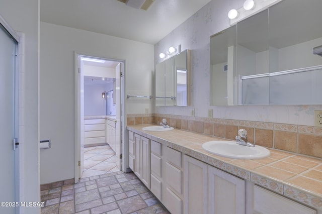 full bath with stone finish floor, a shower with shower door, a sink, and double vanity