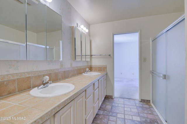 full bathroom with double vanity, stone tile floors, backsplash, and a sink