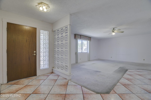 carpeted foyer entrance with a textured ceiling, a ceiling fan, and tile patterned floors