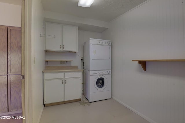 laundry room featuring cabinet space, baseboards, and stacked washer / drying machine