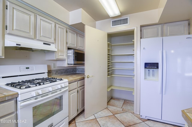 kitchen featuring light tile patterned floors, under cabinet range hood, white appliances, visible vents, and light countertops