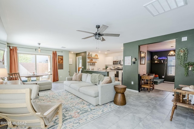 living area with ceiling fan, a wealth of natural light, visible vents, and baseboards