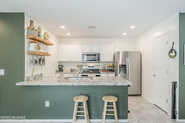 kitchen featuring a peninsula, a sink, visible vents, white cabinetry, and appliances with stainless steel finishes