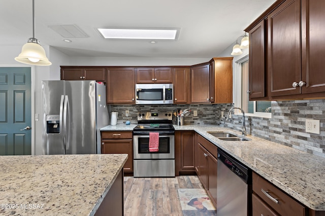 kitchen featuring appliances with stainless steel finishes, light stone counters, a sink, light wood-style floors, and backsplash